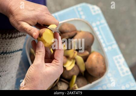Les mains de l'épluchage des pommes de terre avec un couteau de cuisine. Banque D'Images
