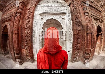 Femme en costume rouge à la recherche à l'ancienne porte de Qutub Minar complexe dans Delhi, Inde Banque D'Images