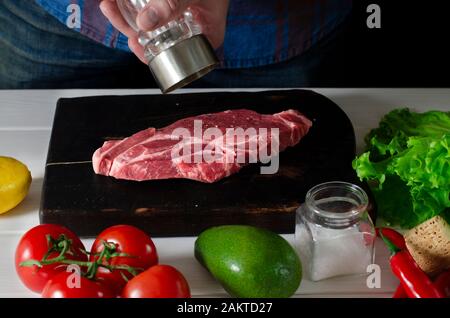 Les mains des hommes cuisinent un steak de viande qui se trouve sur un tableau de découpe Banque D'Images