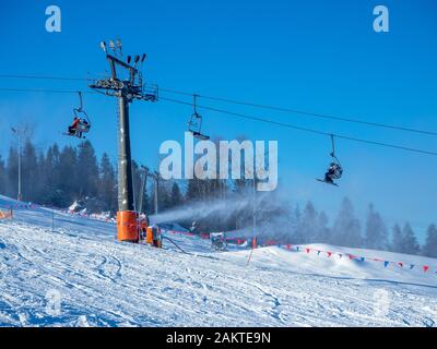 Remontée mécanique (télésiège) avec skieurs, pistes de ski et canons à neige non reconnaissables en action dans la station de ski de Bialka Tatrzanska en Pologne Banque D'Images