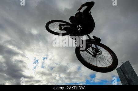 10 janvier 2020, Hessen, Frankfurt/Main : un jeune saute avec son dirtjump vélo sur la facilité de patineur dans le Osthafenpark près de la Banque centrale européenne (BCE) en face d'un ciel nuageux. Photo : Arne Dedert/dpa Banque D'Images