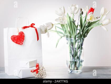 Sac de Shopping, coeur rouge et blanc, ruban et cadeaux bouquet bouquet de tulipes dans un vase sur fond blanc. Banque D'Images