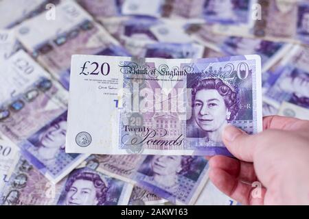 Détenir une note britannique de vingt livres sterling avec plus de notes en arrière-plan Banque D'Images