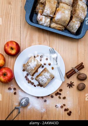 Vue de dessus d'un rouleau apple pie - Strudel aux pommes. Tourte aux pommes, de la cannelle, les noix et les raisins secs, saupoudré de sucre en poudre dans une assiette sur un sol en bois ta Banque D'Images