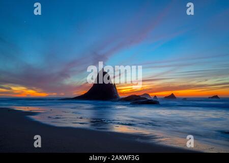 Un coucher de soleil coloré fait marche arrière sur les formations rocheuses uniques de Shark Fin Rock sur la plage de Martin, dans Half Moon Bay, Californie à mesure que les vagues arrivent Banque D'Images