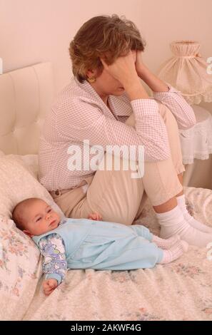 jeune mère avec un bébé souffrant de dépression postnatale, regardant triste, assis sur un lit Banque D'Images