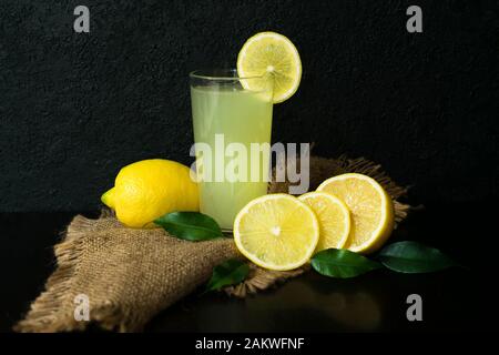 Verre de jus de citron et les citrons sur un fond noir. La vitamine boire. Banque D'Images