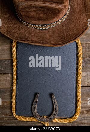 Planche à craie noire lasso fer à cheval et chapeau de cowboy traditionnel sur fond en bois Banque D'Images