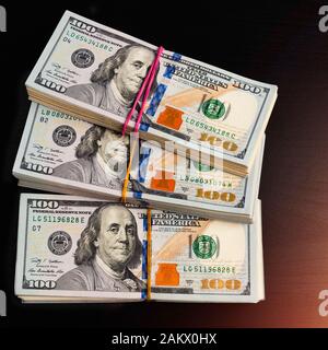 Trois paquets de one hundred dollar bills en espèces sur un tableau sombre. L'éclairage sur le côté Banque D'Images