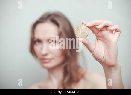 La femme démontre qu'elle tient une bitcoin dans sa main sur un fond de visage. Banque D'Images