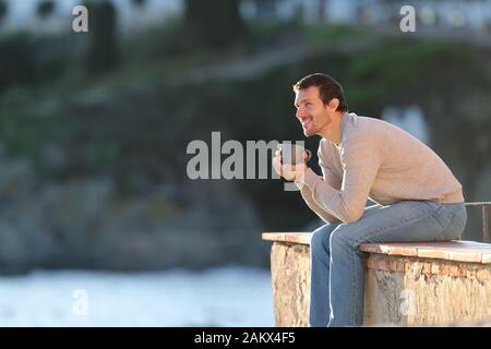 Homme heureux de boire du café en contemplant une vue sur assise dans un balcon en plein air dans une ville de la côte Banque D'Images