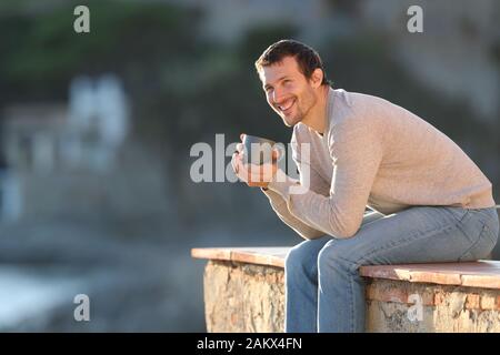 Happy man holding Coffee cup contemplant views assis dans un balcon en plein air dans une ville de la côte Banque D'Images