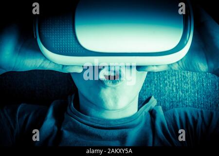 Jeune homme s'amuser avec la technologie de lunettes de réalité virtuelle posée sur le canapé à la maison. Un garçon étonné gestialise le port d'un casque vr. Tech, des vies modernes Banque D'Images