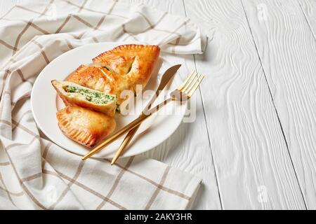 Calzone, pizza fermée aux épinards et au fromage servie sur une plaque blanche avec fourche dorée et couteau sur une table en bois, cuisine italienne, gros plan Banque D'Images