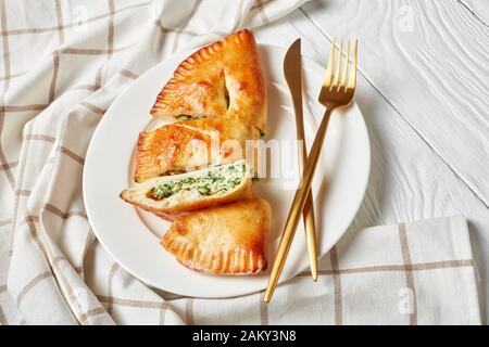 Calzone, pizza fermée aux épinards et au fromage servie sur une plaque blanche avec fourche dorée et couteau sur une table en bois, cuisine italienne, gros plan Banque D'Images