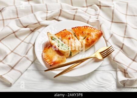 Calzone fraîchement cuit, pizza fermée avec garniture de épinards et de fromage servie sur une plaque blanche avec fourche dorée et couteau sur une table en bois, cuis italien Banque D'Images