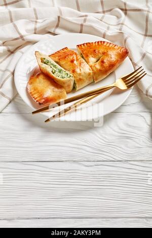 Calzone fraîchement cuit, pizza fermée avec garniture de épinards et de fromage servie sur une plaque blanche avec fourche dorée et couteau sur une table en bois, cuis italien Banque D'Images