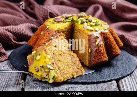 gros plan de gâteau en éponge de carotte de citrouille en tranches avec glaçage orange, parsemé de pistaches sur une plaque noire sur une table en bois rustique Banque D'Images