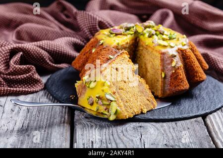 gros plan de gâteau en éponge de carotte de citrouille en tranches avec glaçage orange, parsemé de pistaches sur une plaque noire sur une table en bois rustique Banque D'Images