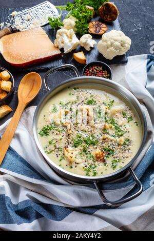 Gros plan de la soupe de chou-fleur à l'ail rôti crémeux avec du fromage asiago dans un bouillon contenant des ingrédients sur une table en béton Banque D'Images