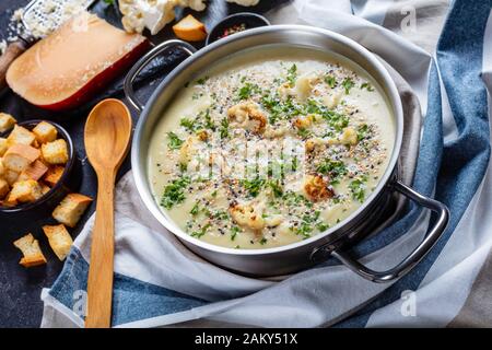 Gros plan de soupe de chou-fleur à l'ail rôti crémeux avec du fromage asiago dans un bouillon contenant des ingrédients et des croûtons sur une table en béton Banque D'Images