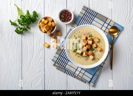 Une portion de soupe de Chou-Fleur à l'ail rôti d'Asiago dans un bol blanc recouvert de croutons, vue horizontale par dessus, plat Banque D'Images