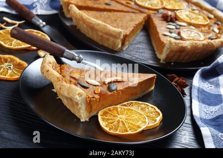 Tranche de tarte aux pommes de terre douces décorée de chips d'orange, de graines de citrouille sur une plaque noire sur une table en bois, vue horizontale d'en haut, gros plan Banque D'Images