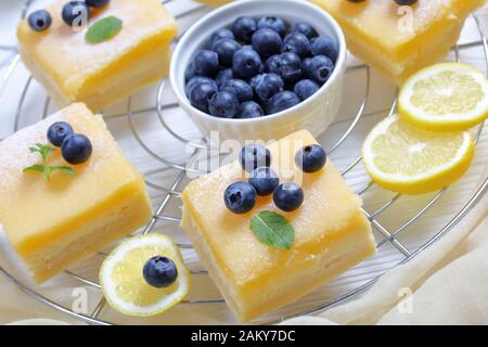 Barres de curd au citron recouvertes de sucre en poudre, de bleuets frais et de feuilles de menthe sur une grille métallique sur une table en bois, gros plan Banque D'Images