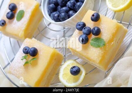 Gros plan de barres de curd de citron surmontées de sucre en poudre, de bleuets frais et de feuilles de menthe sur une grille métallique sur une table en bois Banque D'Images