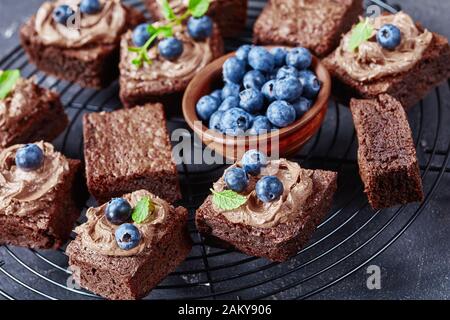 brownies au chocolat maison recouvertes de crème au chocolat et décorées de bleuets frais et de menthe sur un support en fil de fer, gros plan Banque D'Images