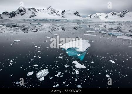 Glace de glacier, glace de brises, icebergs devant les montagnes et les glaciers de la baie du Paradis avec des réflexions de l'océan sur l'atmosphère dominante, Antarctique Banque D'Images