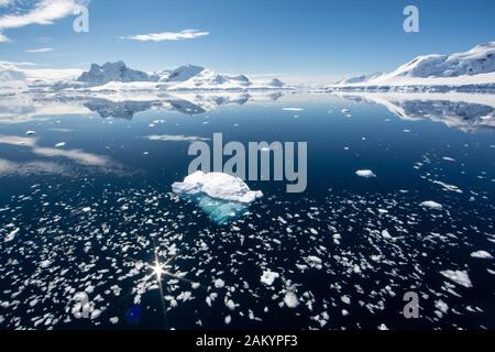 Glace de glacier, glace de brises, glace de mer avec les montagnes et les glaciers de la baie paradisiaque sous un soleil lumineux avec des reflets, Antarctique Banque D'Images