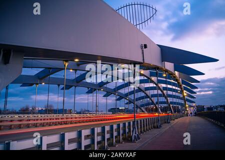 Kotlarski pont suspendu au-dessus de la Vistule à Cracovie, Pologne, contre la lumière au coucher du soleil. Des voitures qui passent sur la route, des sentiers de lumière. Banque D'Images