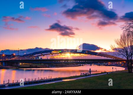 Kotlarski pont suspendu au-dessus de la Vistule à Cracovie, Pologne, contre la lumière de soleil violet et orange avec de l'eau. reflelection Soleil en suspens Banque D'Images