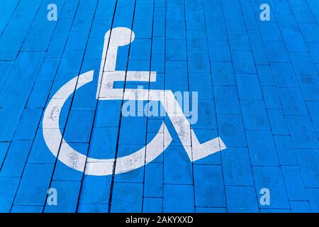 Fauteuil roulant avec panneau d'information sur sol en brique, place de parking pour handicapés. Symbole peint en blanc sur fond bleu. Banque D'Images
