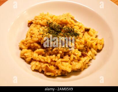 Risotto italien traditionnel aux champignons, safran, persil, dans un plat blanc, table en bois Banque D'Images
