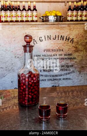 Une bouteille de liqueur de cerise traditionnelle portugaise Ginjinha et deux verres à feu remplis de liqueur et de cerise. Banque D'Images