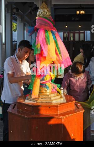 En dehors de Lak Mueang (City Pillar Shrine) à Bangkok, en Thaïlande, les fidèles lient des bandes colorées de tissu autour d'un pilier phallique Banque D'Images