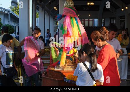 En dehors de Lak Mueang (City Pillar Shrine) à Bangkok, en Thaïlande, les fidèles lient des bandes colorées de tissu autour d'un pilier phallique Banque D'Images