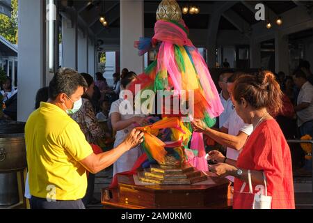 En dehors de Lak Mueang (City Pillar Shrine) à Bangkok, en Thaïlande, les fidèles lient des bandes colorées de tissu autour d'un pilier phallique Banque D'Images