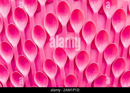 Cuillères roses en plastique dans une rangée sur fond rose. Conception abstraite Banque D'Images