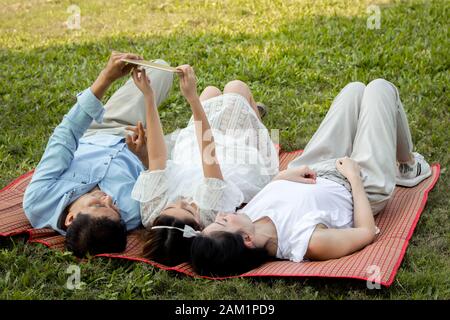 La famille asiatique utilise la tablette sur le tapis. Les filles apprennent à partir d'une tablette que les parents enseignent. Les parents et les enfants jouent à la tablette Banque D'Images