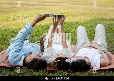La famille asiatique utilise la tablette sur le tapis. Les filles apprennent à partir d'une tablette que les parents enseignent. Les parents et les enfants jouent à la tablette Banque D'Images