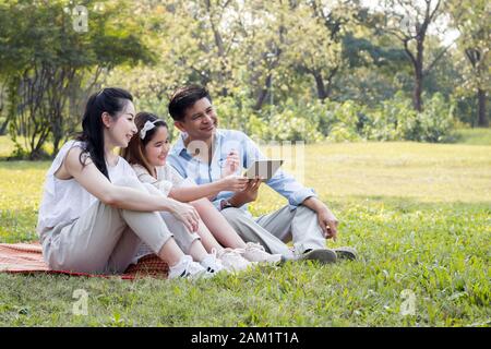 La famille asiatique utilise la tablette sur le tapis. Les filles apprennent à partir d'une tablette que les parents enseignent. Banque D'Images
