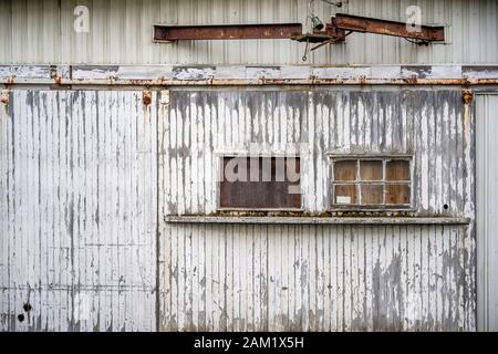 Fenêtres fermées par un morceau de contreplaqué sur la porte en bois sur rouleau coulissant gainée de lamelles avec mur de peinture décollement d'un ancien entrepôt industriel b Banque D'Images