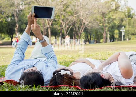 La famille asiatique utilise la tablette sur le tapis. Les filles apprennent à partir d'une tablette que les parents enseignent. Les parents et les enfants jouent à la tablette Banque D'Images