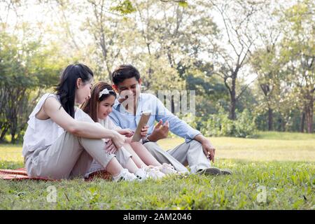 La famille asiatique utilise la tablette sur le tapis. Les filles apprennent à partir d'une tablette que les parents enseignent. Banque D'Images