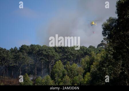 La lutte contre l'hélicoptère pompiers jaune feu de forêt en Côte d'Astoria, Espagne Banque D'Images