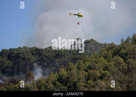 La lutte contre l'hélicoptère pompiers jaune feu de forêt en Côte d'Astoria, Espagne Banque D'Images