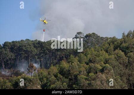 La lutte contre l'hélicoptère pompiers jaune feu de forêt en Côte d'Astoria, Espagne Banque D'Images